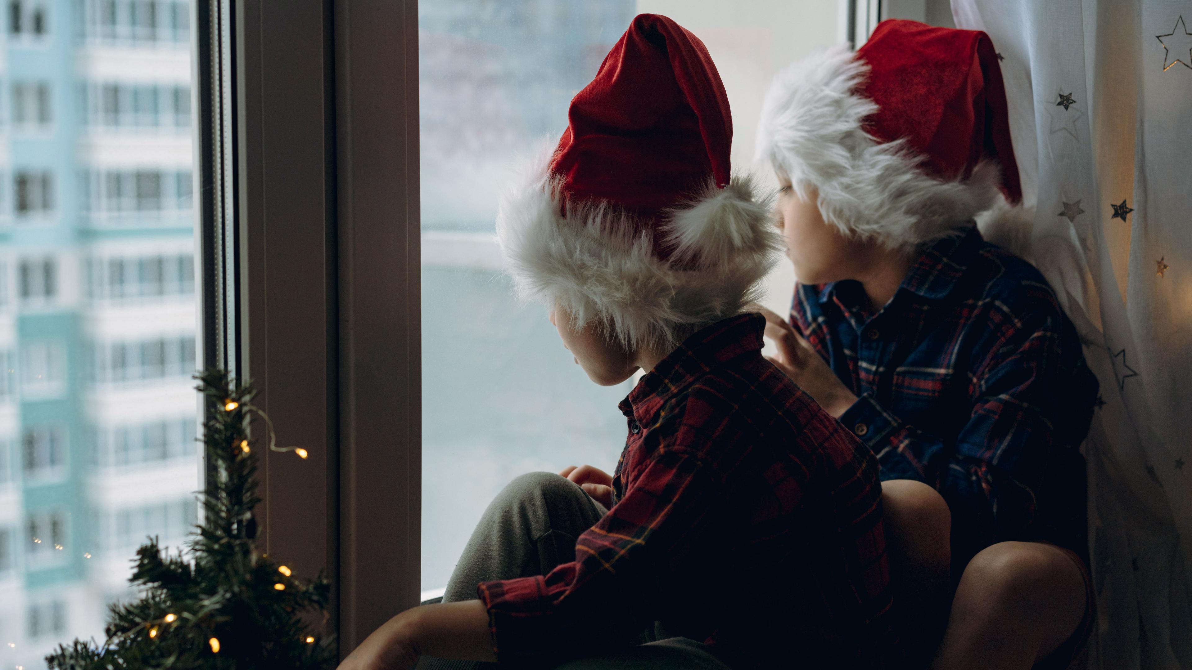 Kinder tragen Santa Hüte und karierten Hemden sitzen umarmt durch das Fenster warten auf Weihnachten. 
