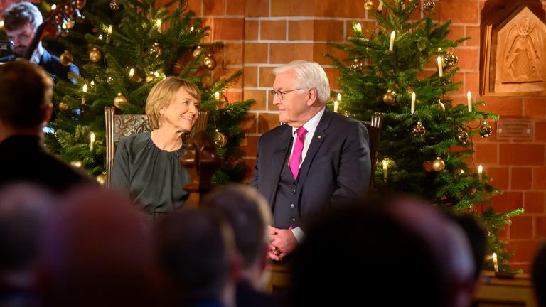 "Weihnachten mit dem Bundespräsidenten": Bundespräsident Frank-Walter Steinmeier sitzt neben seiner Ehefrau Elke Büdenbender in der Kirche vor geschmückten Weihnachtsbäumen.