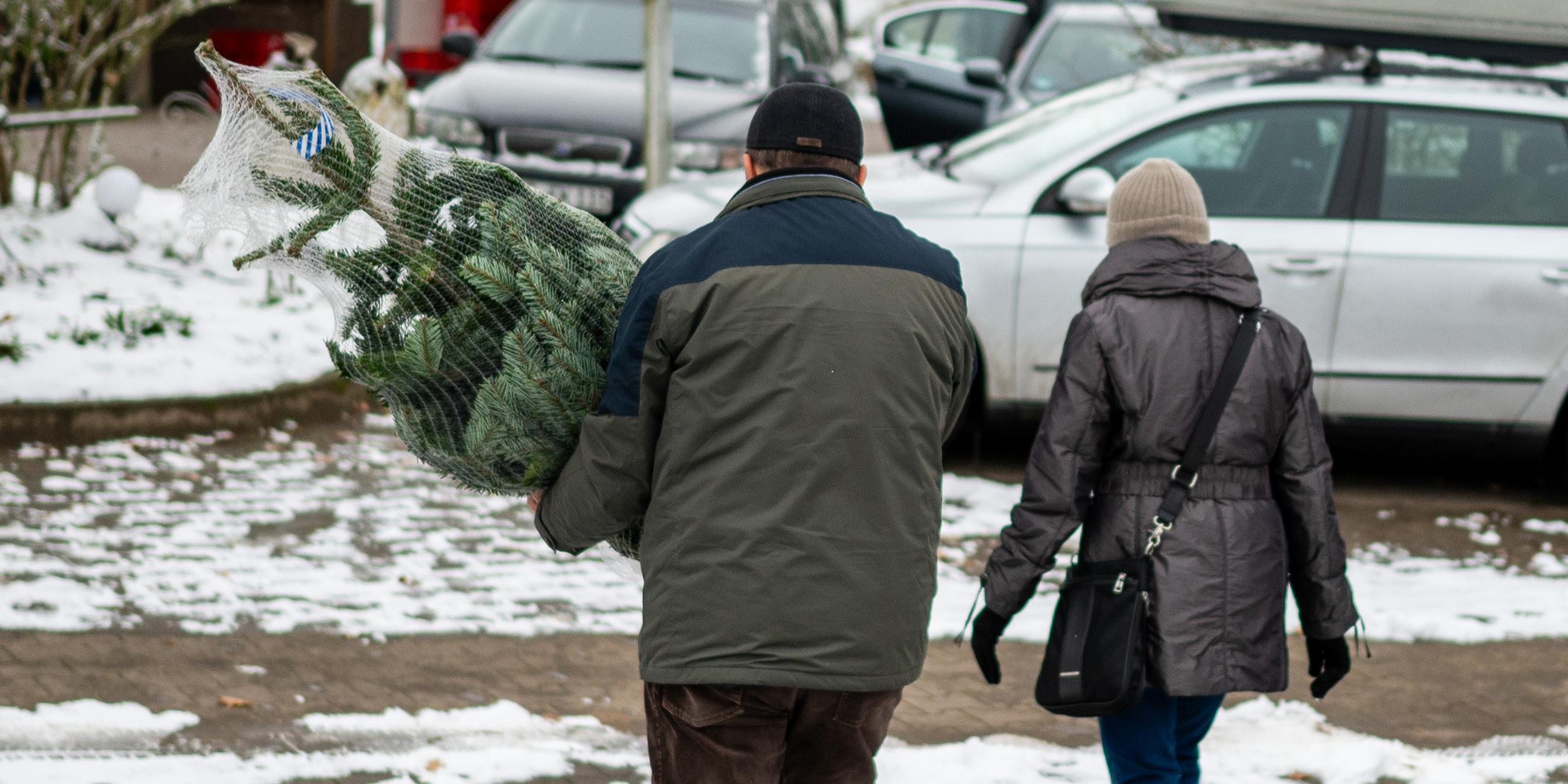Zwei Kunden gehen mit eigenem Weihnachtsbaum zum Auto. 