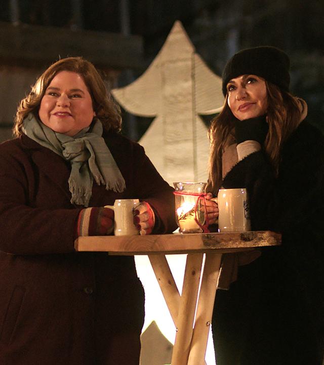 Katja Baumann (Simone Thomalla) und Leslie Wolff (Nadine Wrietz) stehen winterlich gekleidet, bei romantischer Beleuchtung, an einem Holztisch auf dem Weihnachtsmarkt.