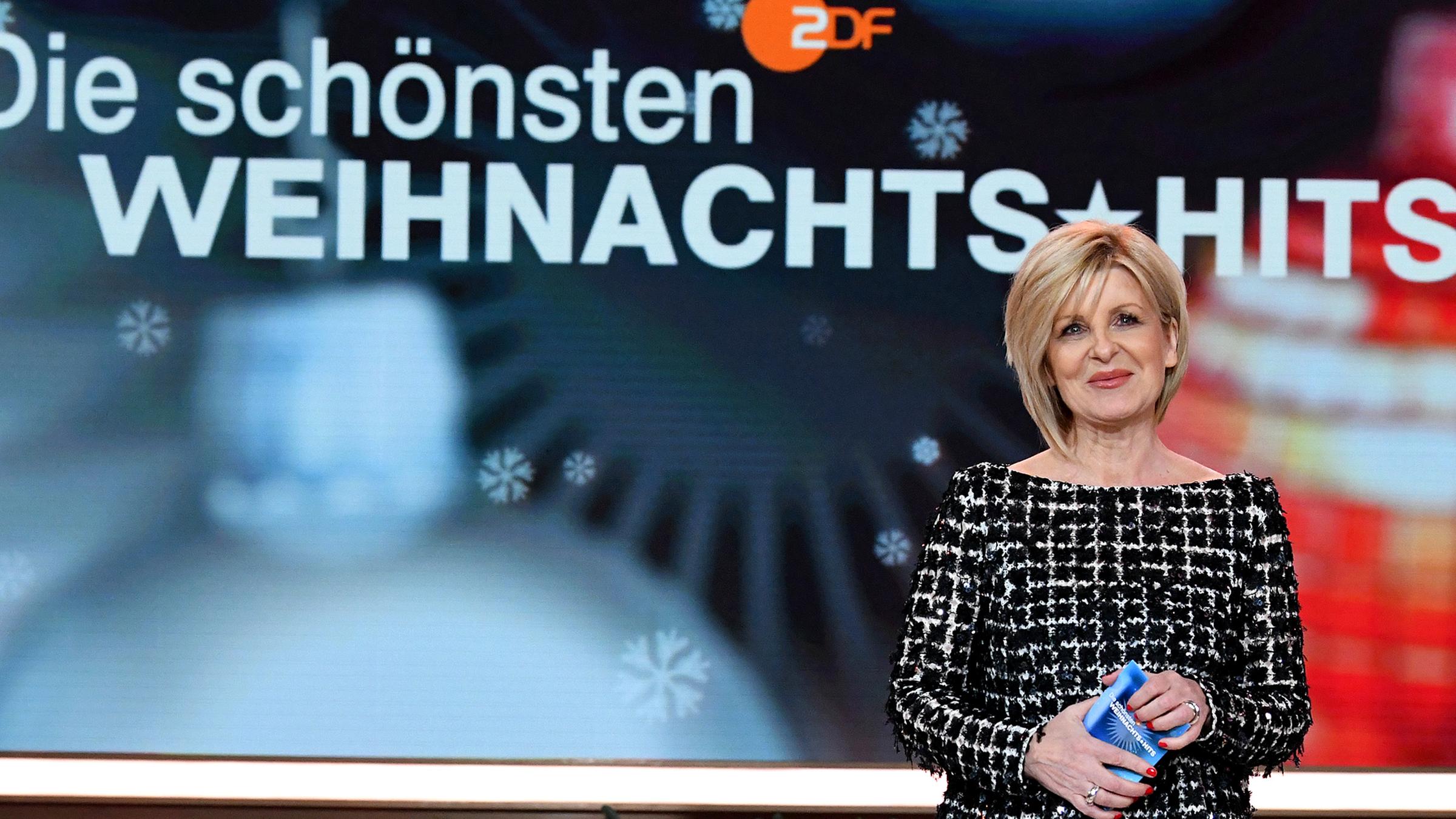 Carmen Nebel steht in der Studiodekoration und schaut in die Kamera.