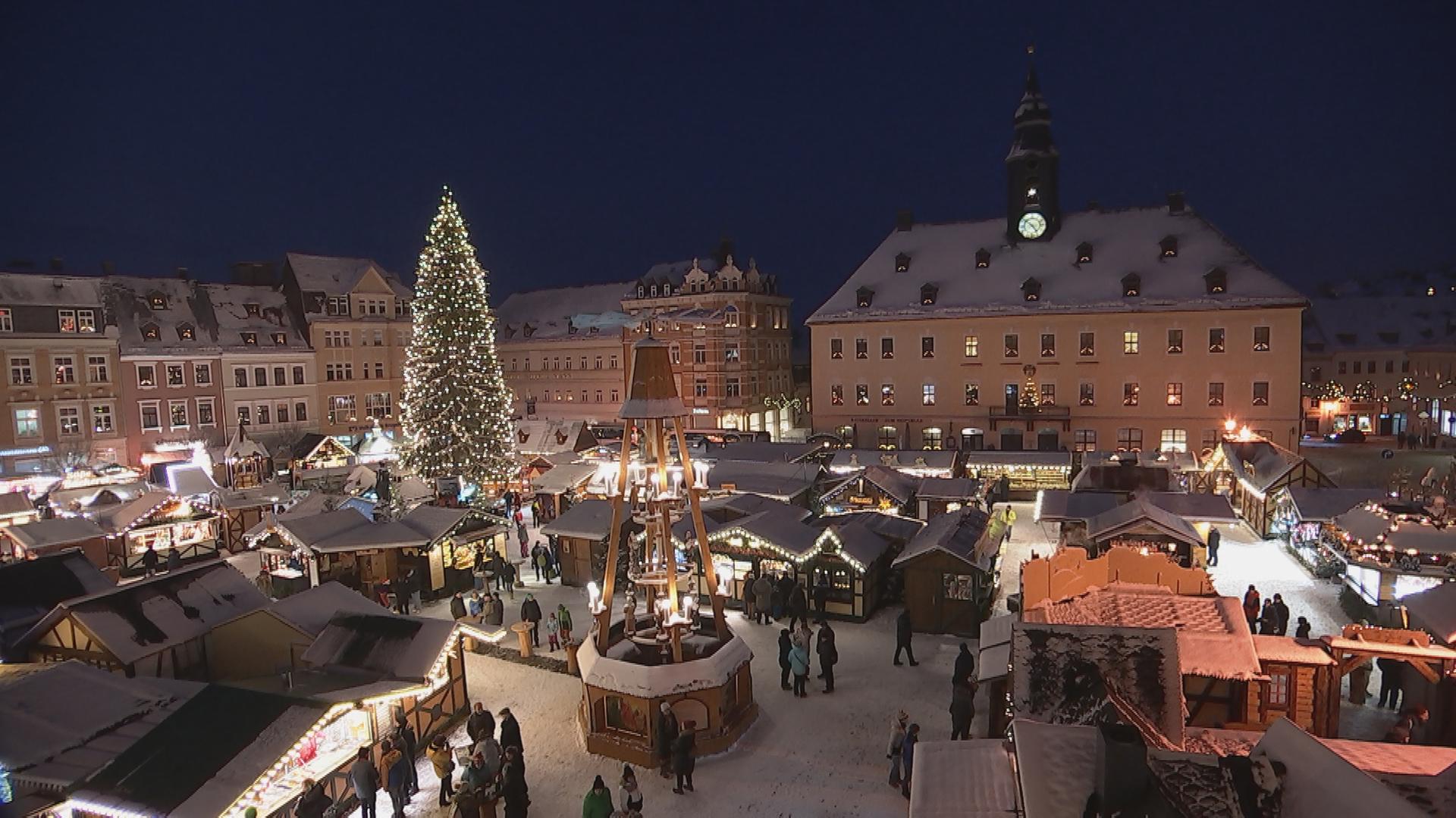 Weihnachtsmarkt in Annaberg-Buchholz bei Nacht. Schneebedeckter Platz mit Buden, großem Weihnachtsbaum und Weihnachtsmühle.