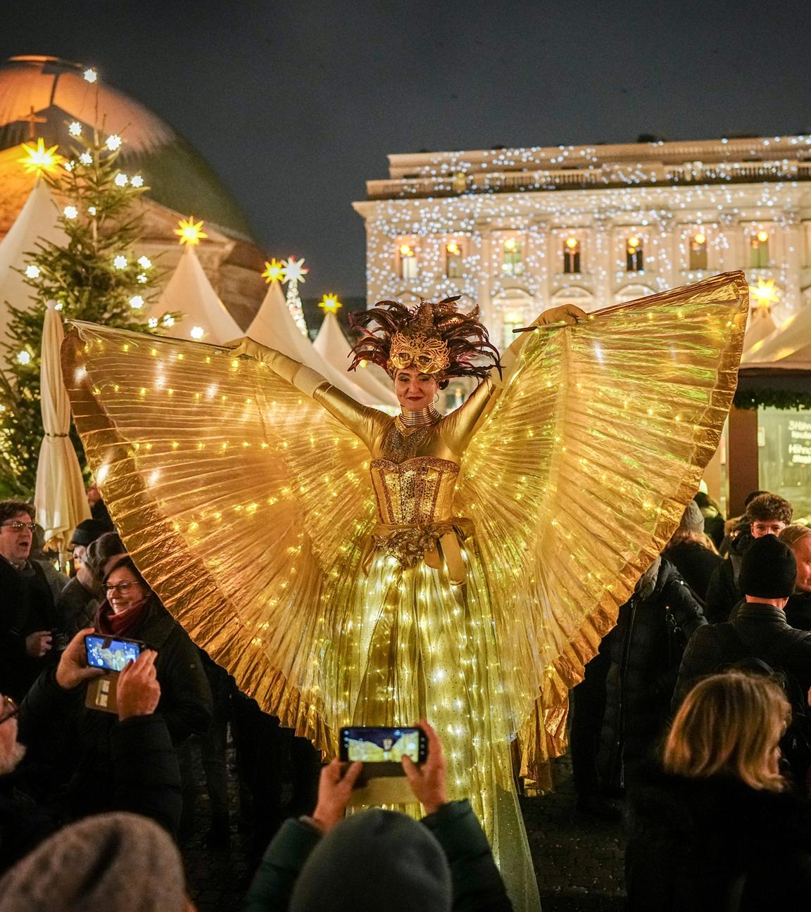 Als leuchtender Engel verkleidet geht eine Darstellerin auf Stelzen über den Weihnachtsmarkt am Bebelplatz in der Nähe des Gendarmenmarktes am 03.12.2023.