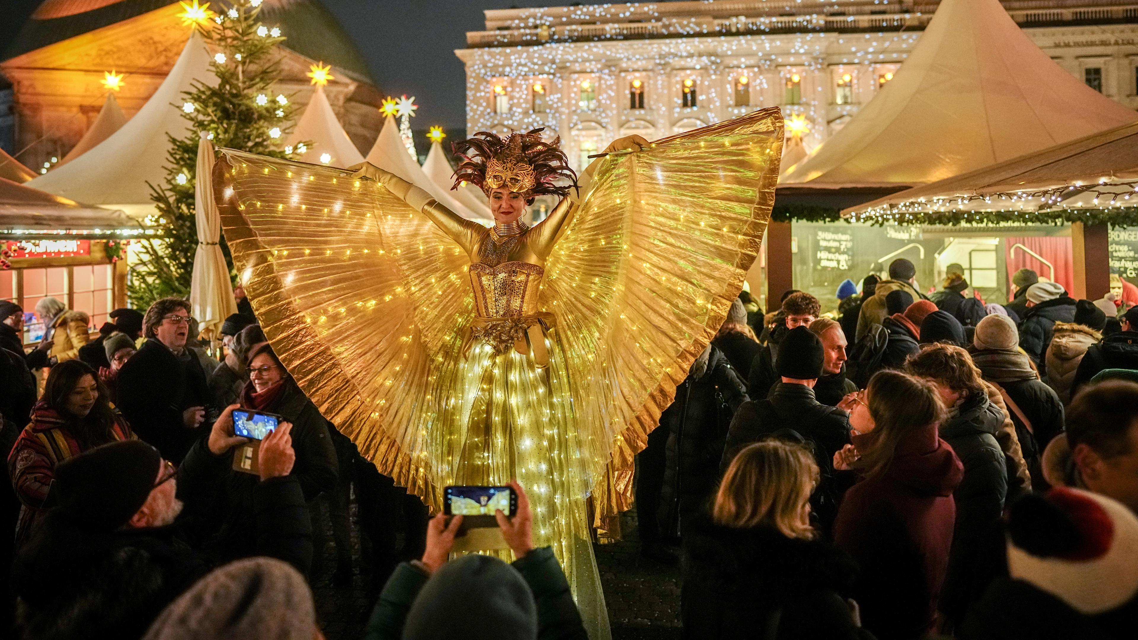 Als leuchtender Engel verkleidet geht eine Darstellerin auf Stelzen über den Weihnachtsmarkt am Bebelplatz in der Nähe des Gendarmenmarktes am 03.12.2023.