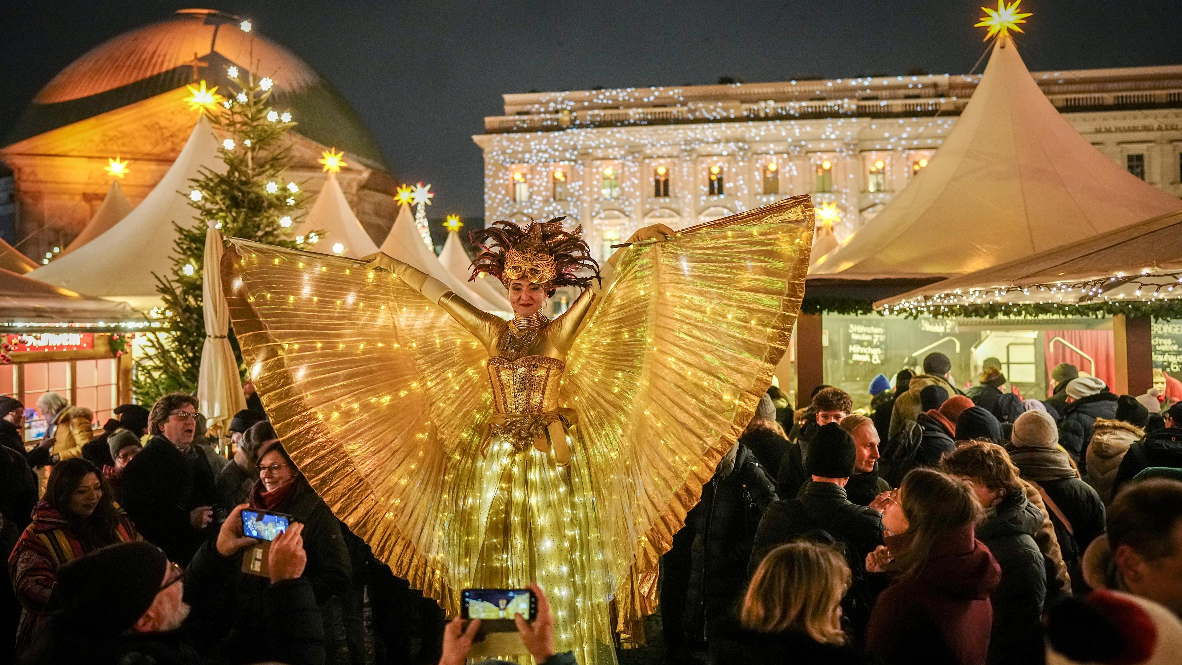 Als leuchtender Engel verkleidet geht eine Darstellerin auf Stelzen über den Weihnachtsmarkt am Bebelplatz in Berlin. 