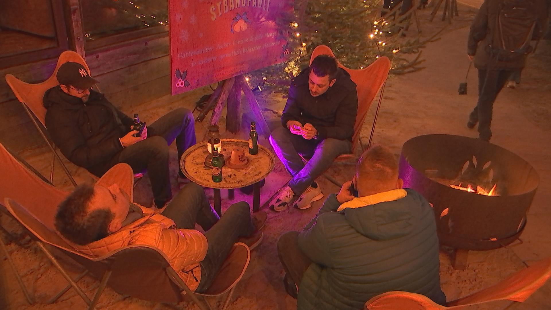 Vier Männer sitzen am Elbstand in Hamburg um einen Tisch und trinken Bier