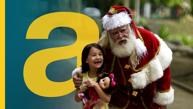 Weihnachtsmann legt Arm um ein kleines Mädchen, das lachend eine Puppe im Arm hält