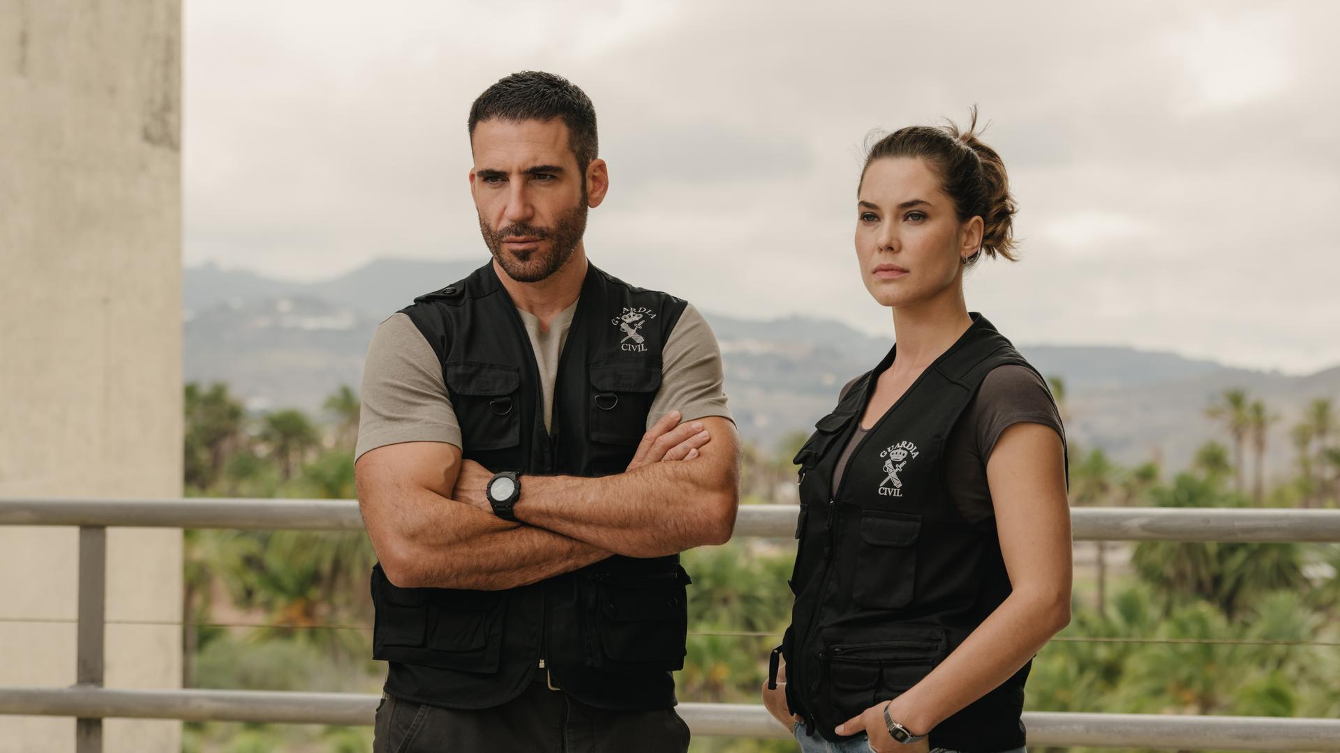 "Weiss & Morales": Raúl Morales (Miguel Ángel Silvestre) und Nina Weiss (Katia Fellin) stehen in schwarzen Westen der Guardia Civil gekleidet nebeneinander vor einem Geländer..