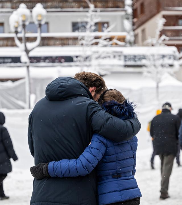 Trauernde Menschen stehen vor der mit Schnee und weissen Folien bedeckte Bar, wo das für viele tödliche Feuer ausgebrochen war