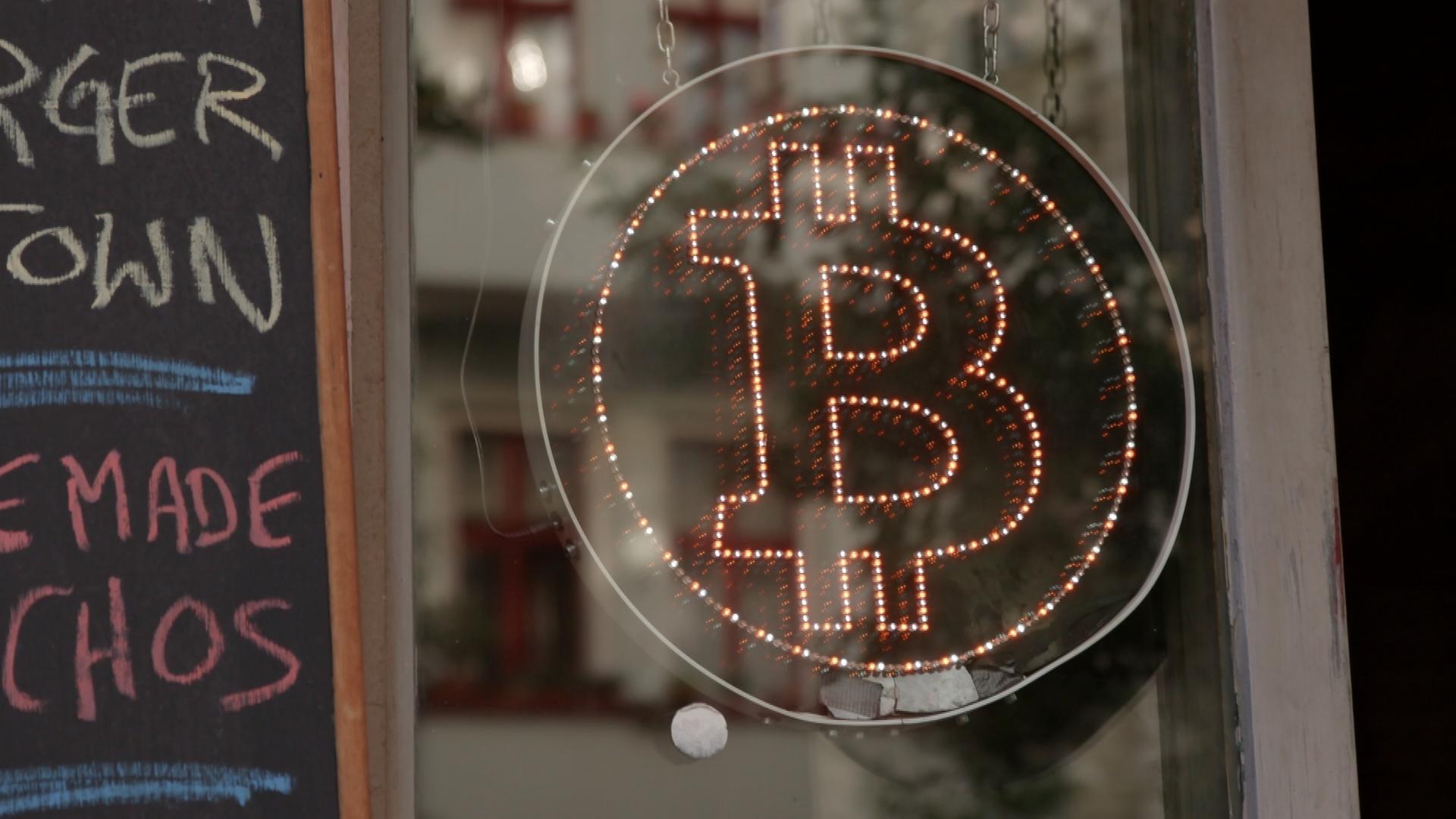 "Welt ohne Banken? - Die Blockchain-Revolution": Lichtreklame mit Bitcoin-Logo.