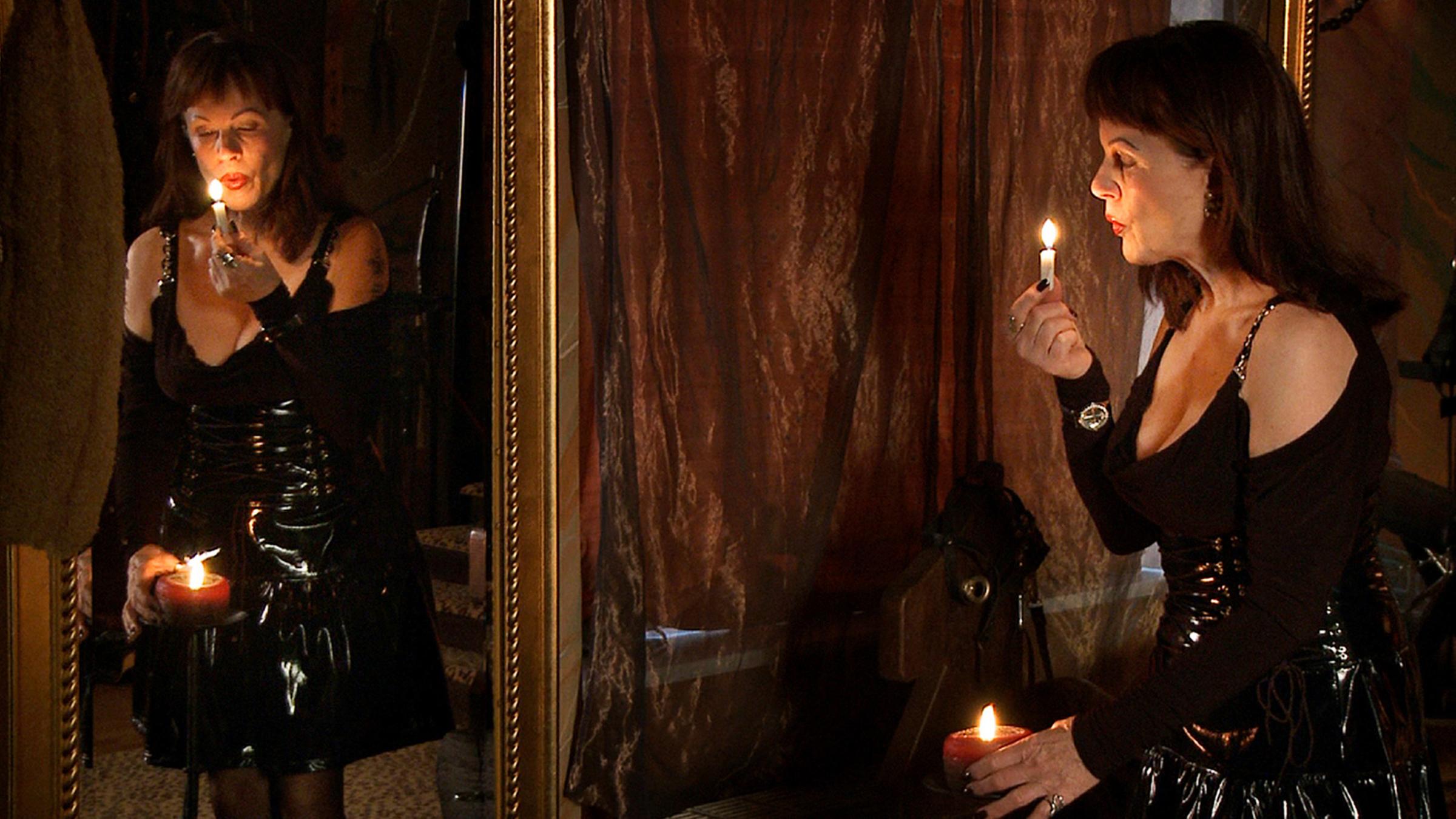 Die gelernte Rentenberaterin und Hypothekenfinanzierungsexpertin Karolina (64) trägt ein schwarzes Lackkleid. In ihrer rechten Hand hält sie eine brennende Kerze, die sie gerade dabei ist, auszupusten.