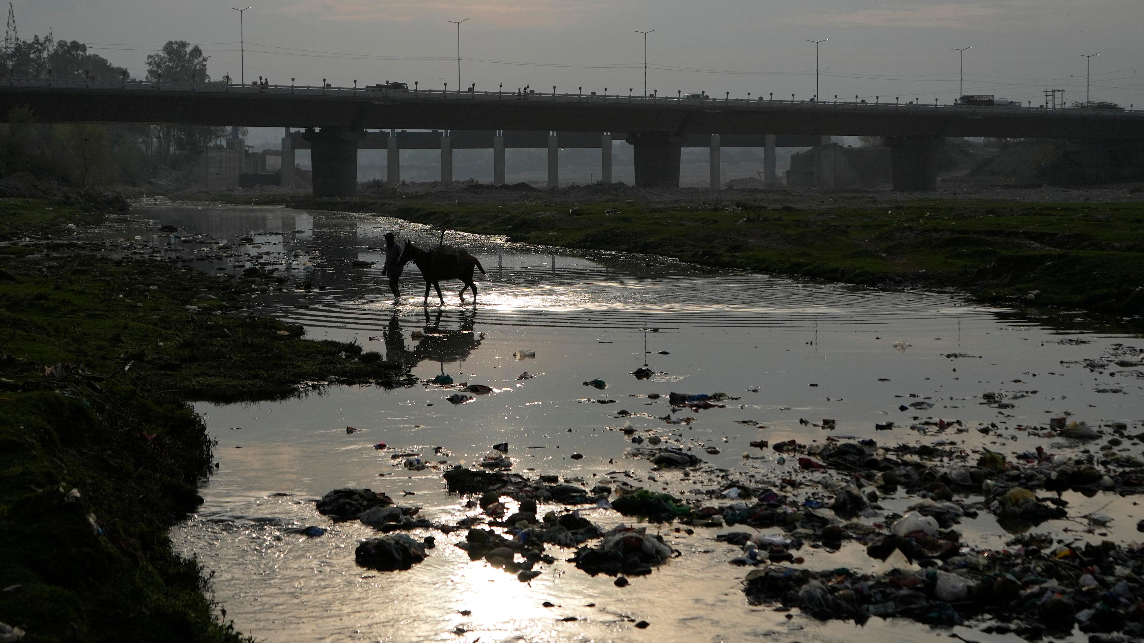 Ein Mann auf einem Pferd trägt am Vorabend des Weltwassertages Sand von den Ufern des verschmutzten Flusses Tawi.