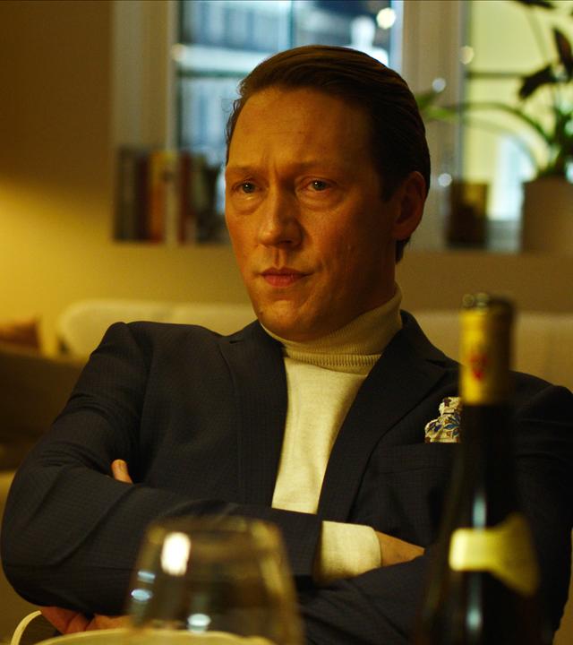 "Exit - Wenn die Welt verschwindet": Adam (Simon J. Berger) sitzt mit verschränkten Armen am Esstisch und schaut sie ernst an.