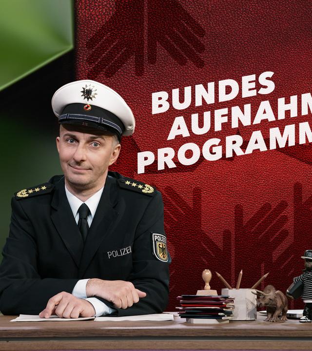 Jan Böhmermann sitzt in einer Polizeiuniform am Schreibtisch. Rechts neben ihm ist das Wort "Bundesaufnahmeprogramm" zu sehen.