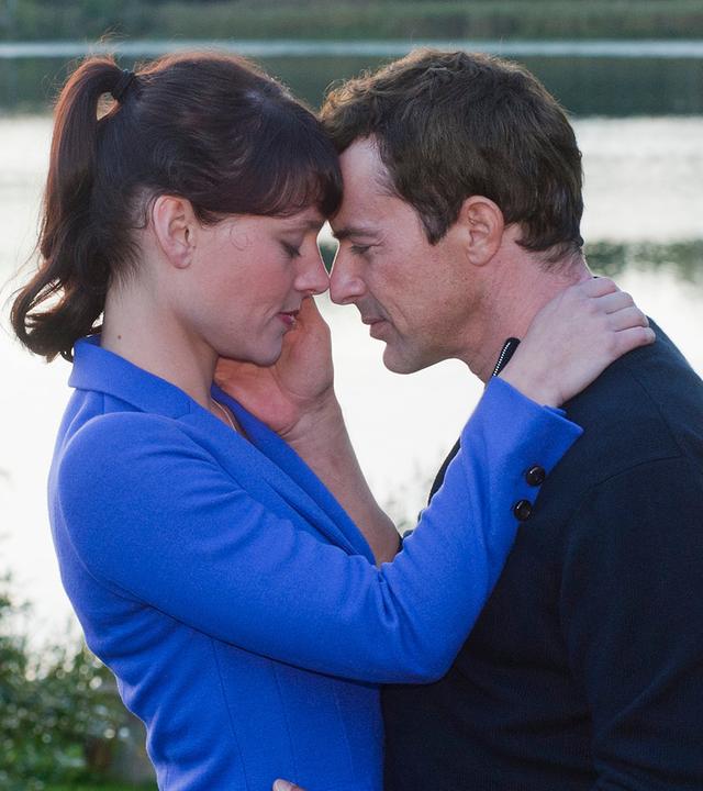 Pernilla (Maike Möller-Bornstein) und Jasper (Gedeon Burkhard) stehen sich umarmend auf einer Wiese vor einem See.