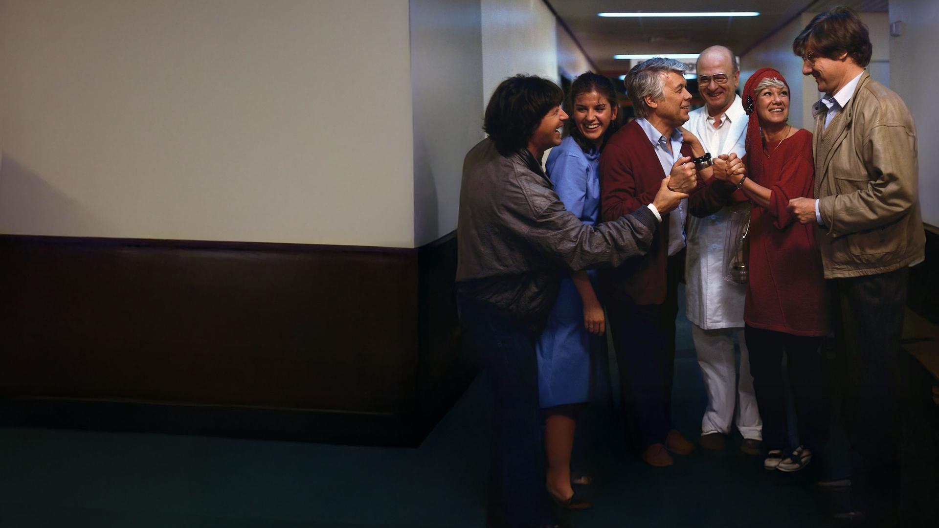 Eine Gruppe lächelnder Menschen schart sich um Werner. Dieser lächelt auch und alle scheinen sich über etwas zu freuen.