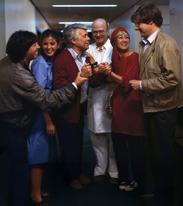 Eine Gruppe lächelnder Menschen schart sich um Werner. Dieser lächelt auch und alle scheinen sich über etwas zu freuen.