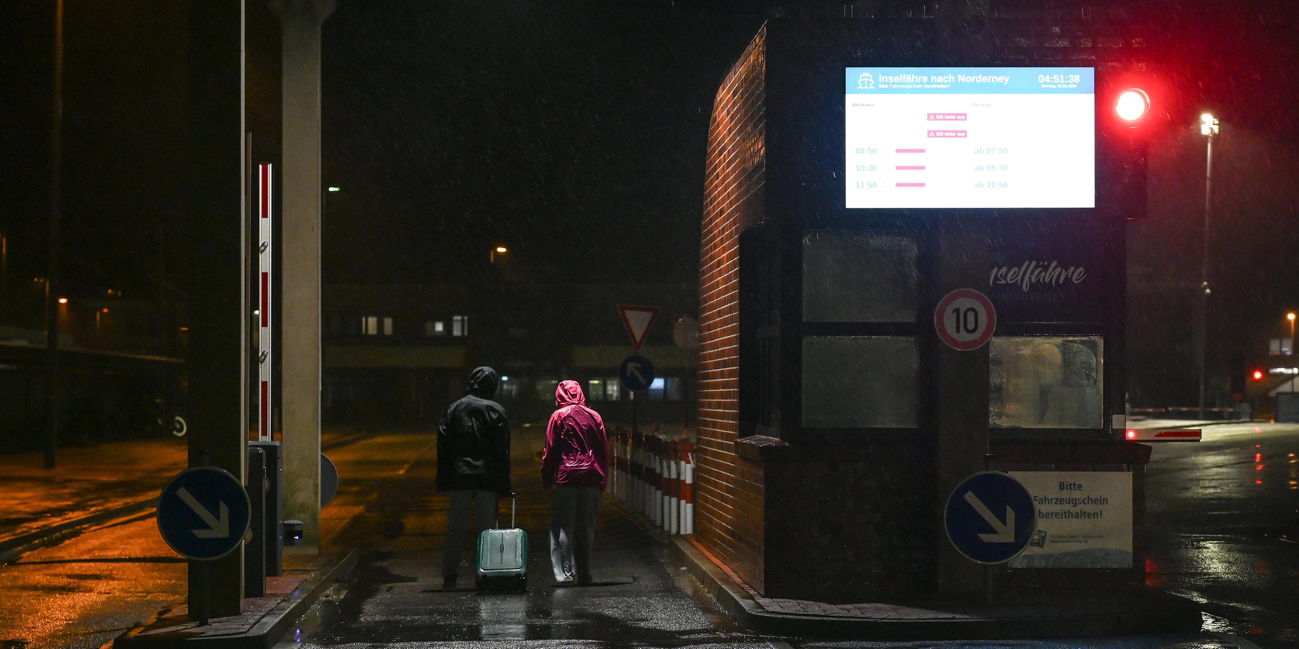 Zwei Fahrgäste der Fähre nach Norderney laufen bei Regen zum Anleger, aufgenommen am 22.01.2024 in Norddeich