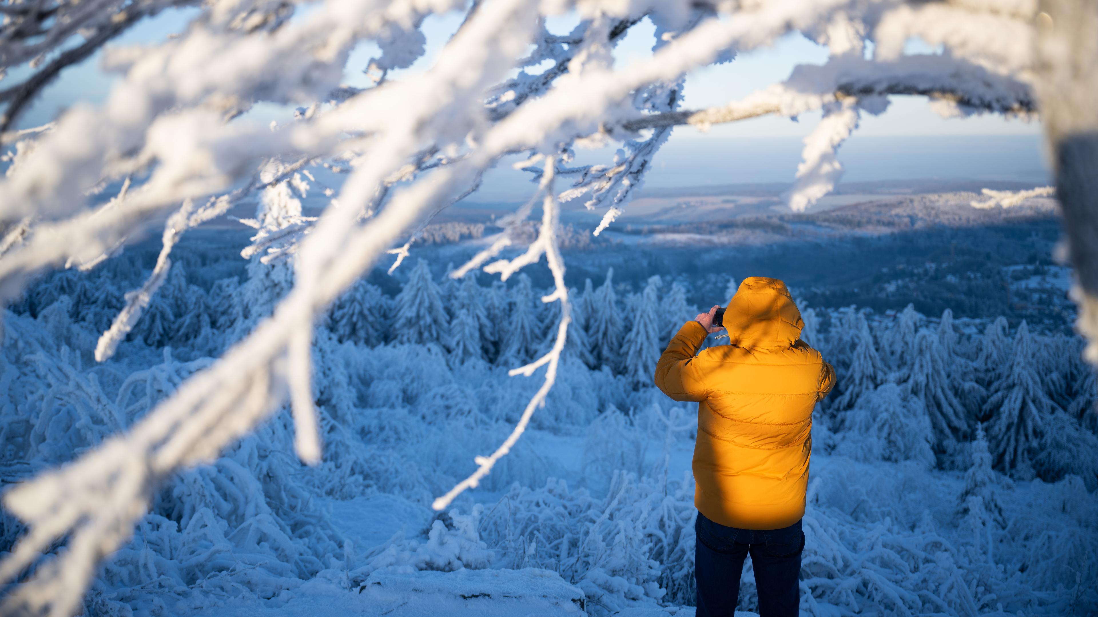 Ein Mann macht auf dem Großen Feldberg am Morgen ein Foto des Taunus während er von der Sonne angestrahlt wird, aufgenommen am 13.12.2022