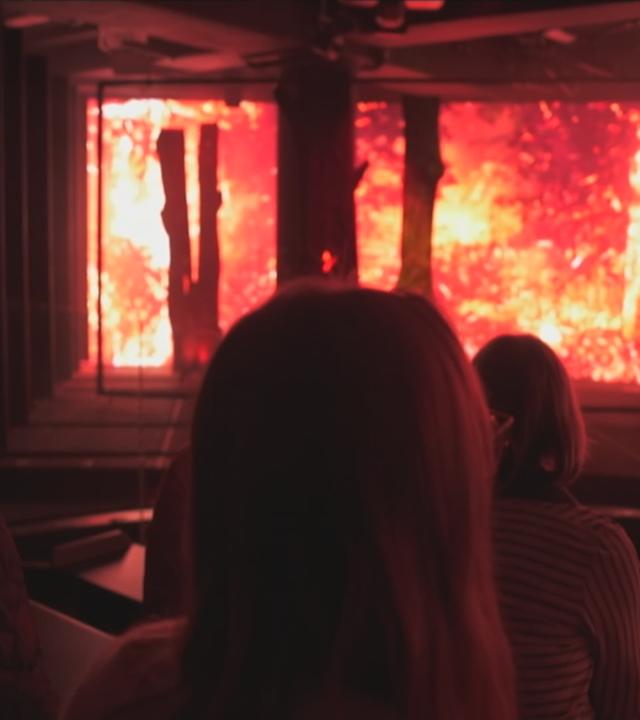 Besucher in der Ausstellung "Wetterextreme" vor einem brennenden Bereich