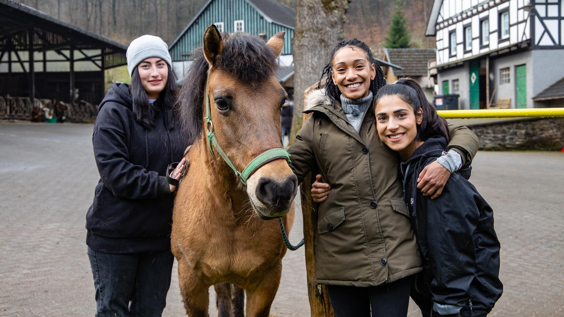 Alina, Feli und Hilla stehen zusammen mit einem Pferd auf dem Hof