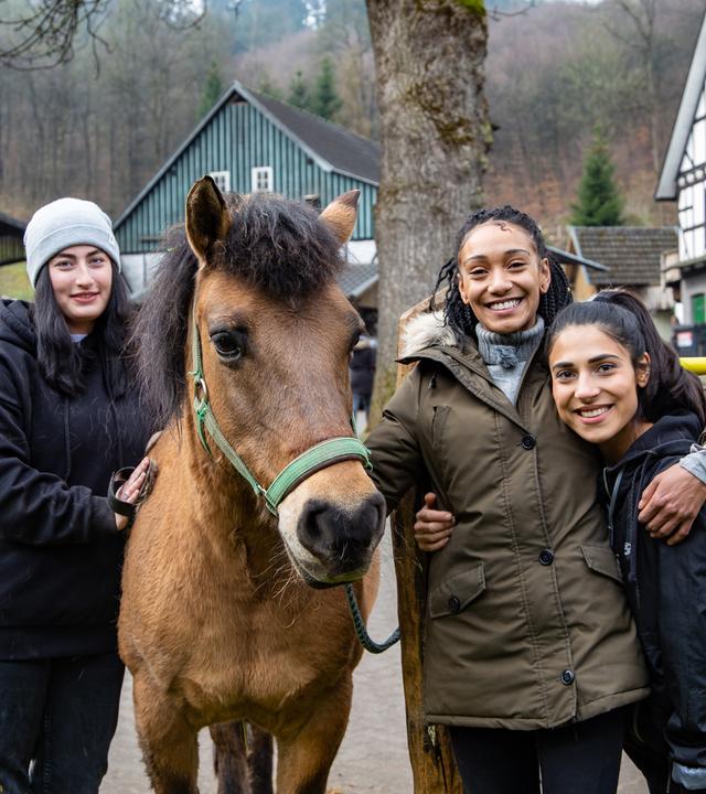 Alina, Feli und Hilla stehen zusammen mit einem Pferd auf dem Hof