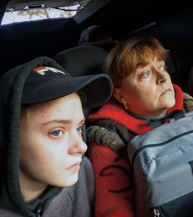 Mutter Natalya sitzt mit Rucksack auf dem Schoß, neben ihrer Tochter Eleni und einem Fahrer im Auto des Evakuierungsteams.