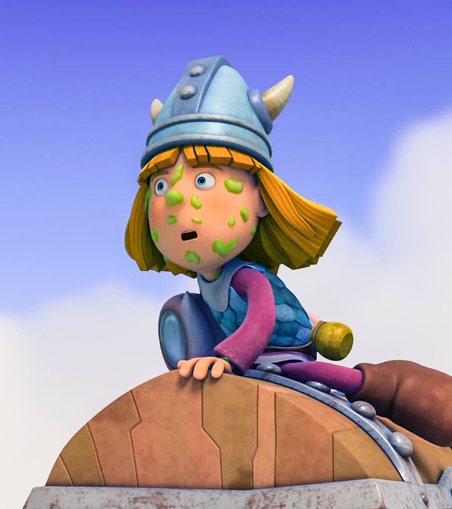 Wickie sitzt auf der Schatzkiste. Dabei hat er etwas Grünes im Gesicht kleben und schaut gespannt in die Ferne. 