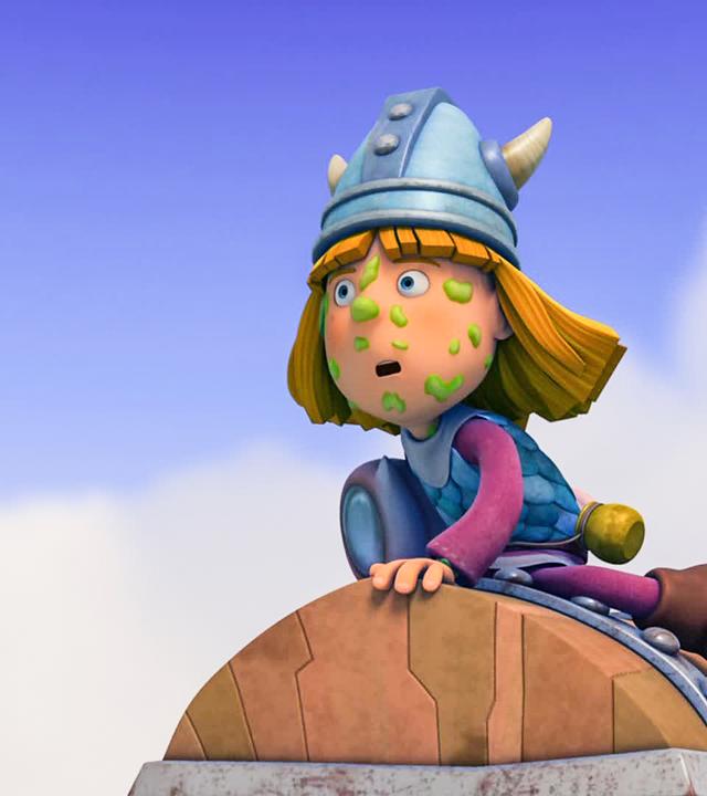 Wickie sitzt auf der Schatzkiste. Dabei hat er etwas Grünes im Gesicht kleben und schaut gespannt in die Ferne. 