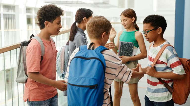 Schülerinnen und Schüler im Alter von ca. 11-13 mit Rucksäcken und teils mit Schulheften stehen beieinander und besprechen sich