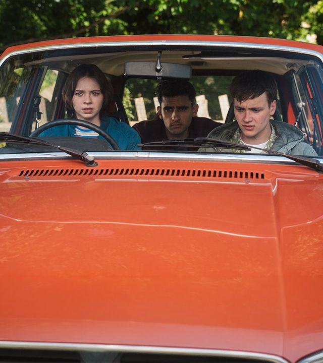 "A Good Girl’s Guide to Murder – Wie man einen Catfish angelt": Pip Fitz-Amobi (Emma Myers) sitzt am Steuer eines roten Autos, neben ihr sitzt Connor Reynolds (Jude Morgan-Collie), auf dem Rücksitz Ravi Singh (Zain Iqbal). Alle drei blicken angespannt nach vorn.