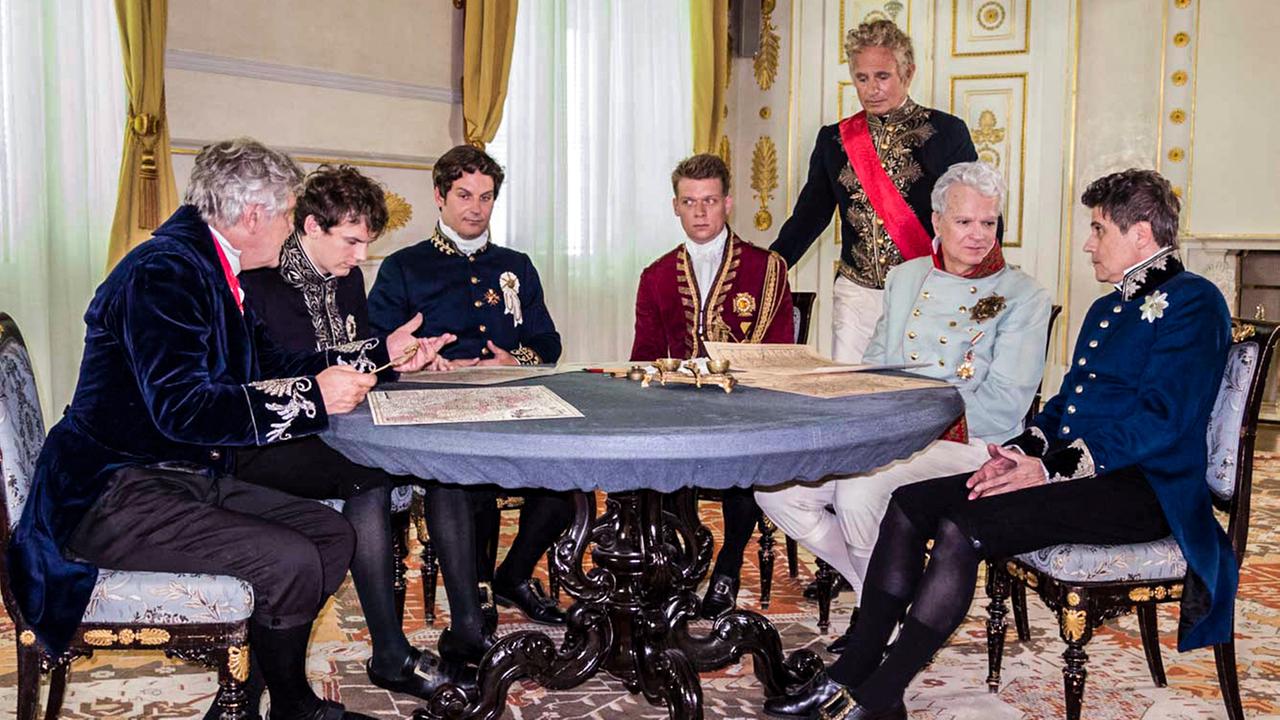 Mäner in historischen Uniformen um einen Tisch sitzend.
