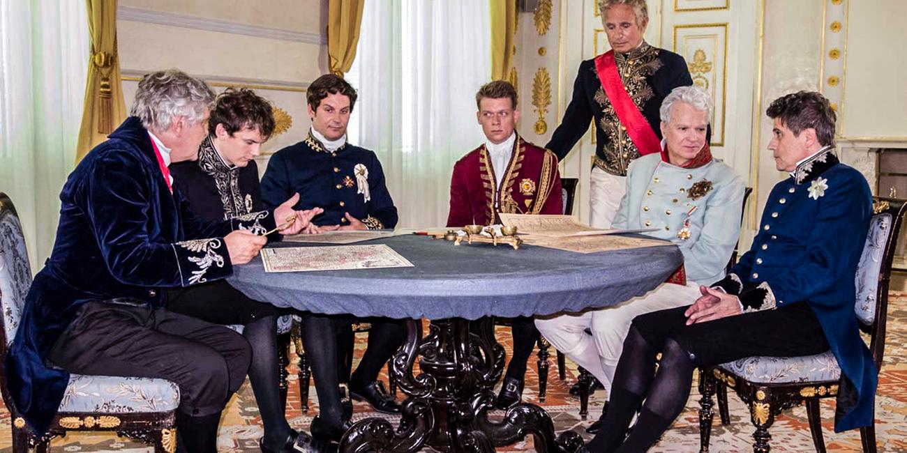 Mäner in historischen Uniformen um einen Tisch sitzend.