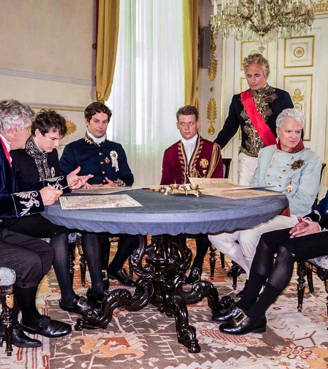 Mäner in historischen Uniformen um einen Tisch sitzend.