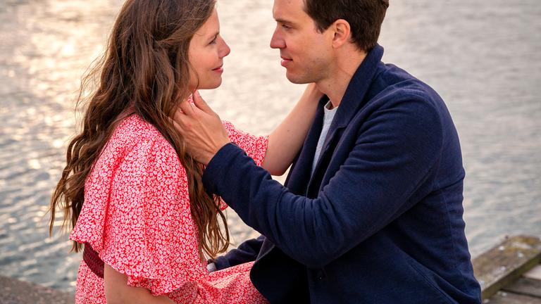 Clara (Leonie Rainer) und Erik (Tobias van Dieken) sitzen an einem Gewässer und blicken sich intensiv an. Beide berühren den Hals des anderen, es scheint, als küssten sie sich gleich.