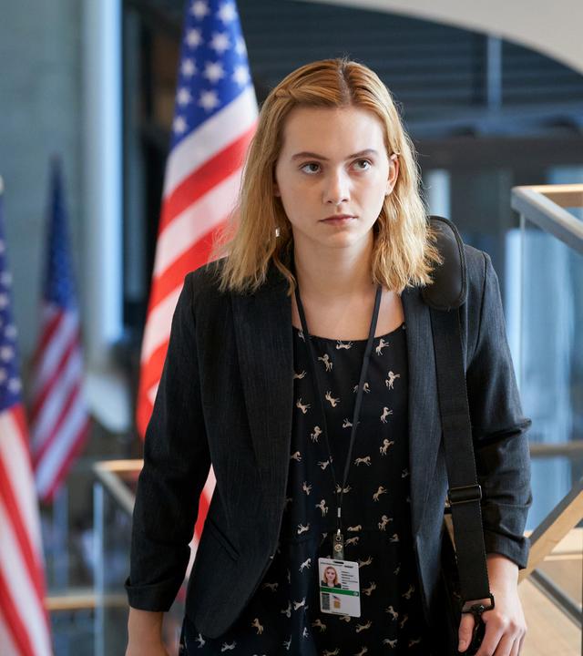 "Winner": Reality (Emilia Jones) steigt in einem Bürogebäude, in dem auf mehreren Stockwerken Fahnen der USA aufgestellt sind, mit einem Mitarbeiterausweis um ihren Hals eine Treppe hinauf.