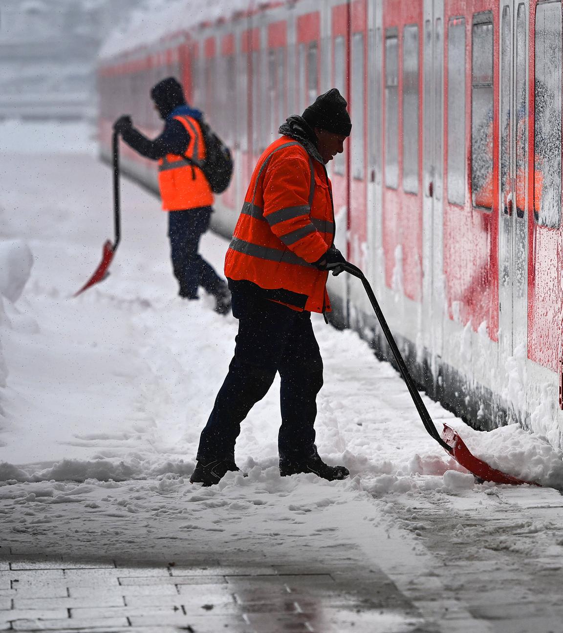 Arbeiter räumt vor einem S-Bahn Zug auf einem Bahnsteig Schnee