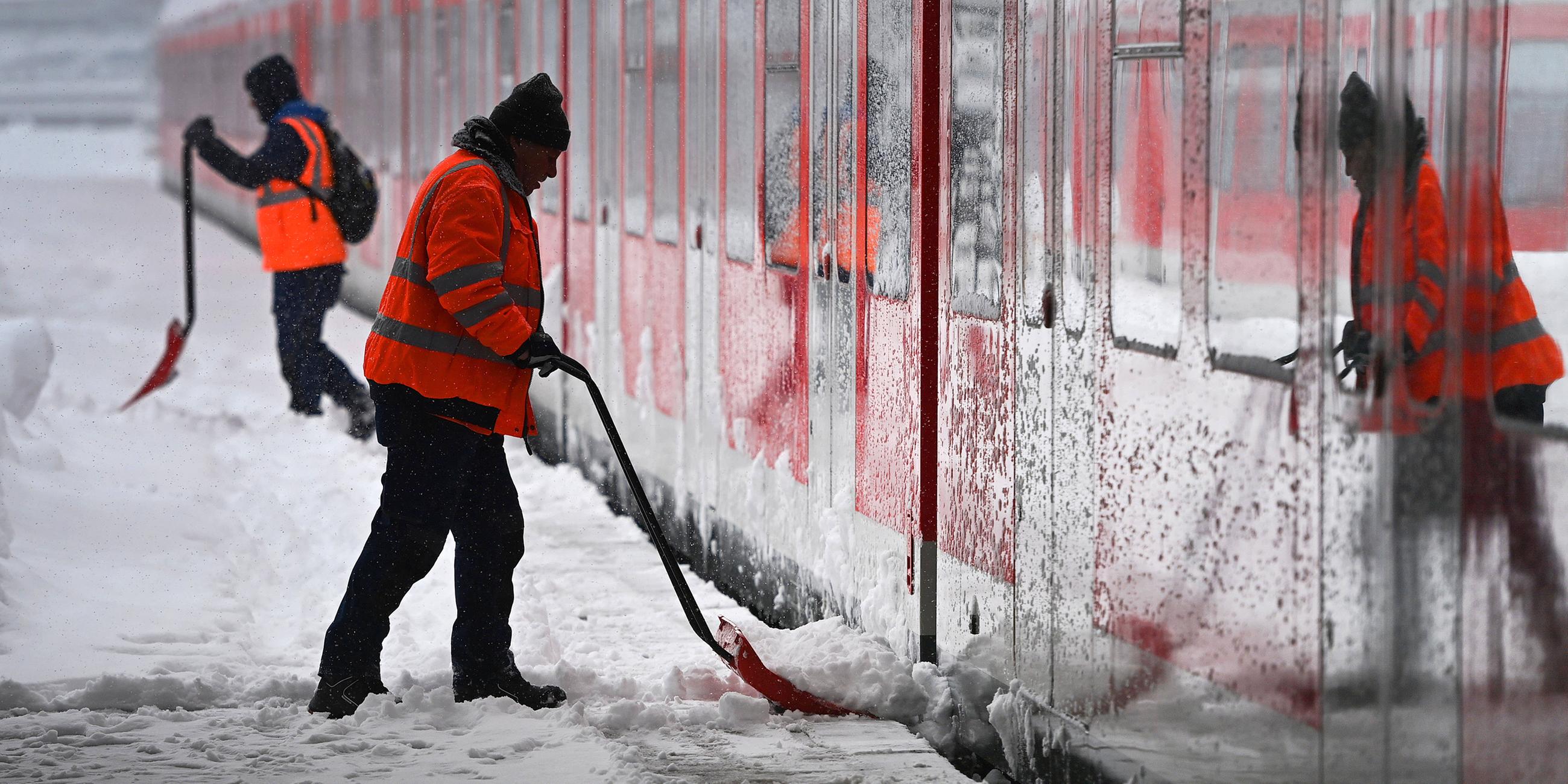 Arbeiter räumt vor einem S-Bahn Zug auf einem Bahnsteig Schnee