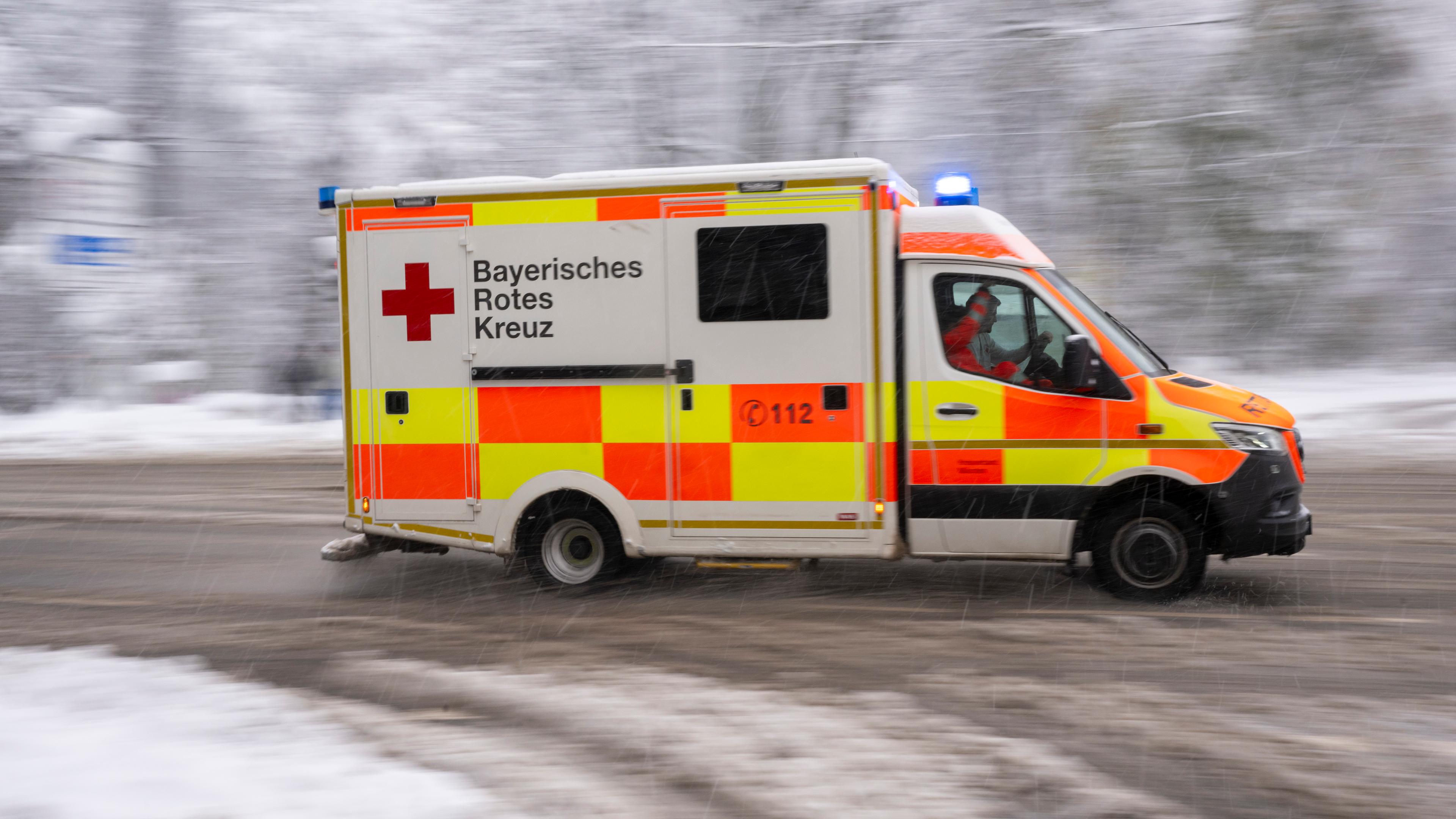 Ein Rettungswagen fährt mit Blaulicht und Martingshorn über eine verschneite Straße in München am 02.12.2023.