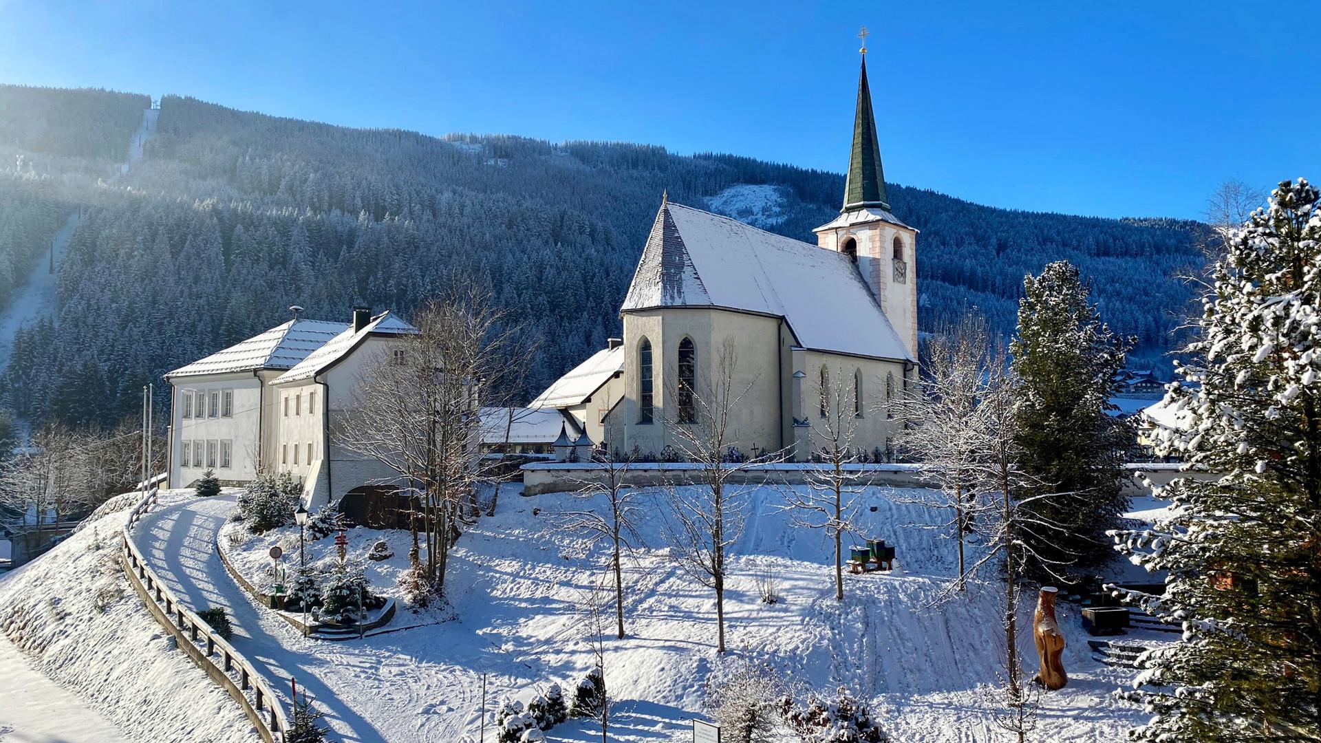 Eine Kirche und Häuser verschneit vor blauem Himmel