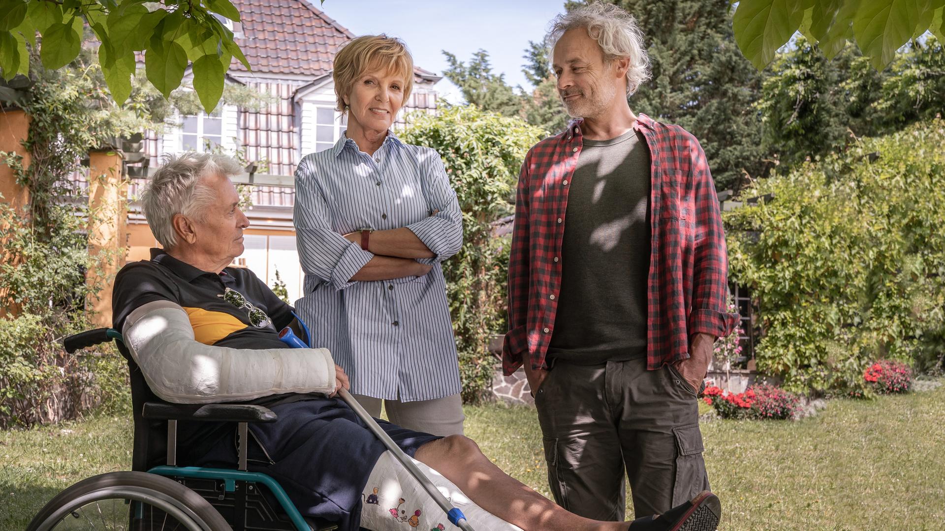 "Wir bleiben Freunde": Volker (Henry Hübchen) sitzt im Rollstuhl im Garten und schaut zu Dorothee (Ulrike Kriener) und Moritz (Marcel Hensema) hinauf. Im Hintergrund das Wohnhaus.
