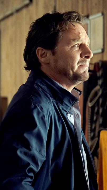 Im Profil: Frank Lechner (Felix Klare) steht mit verzweifeltem Gesichtsausdruck in einem Stall und blickt ins Leere.
