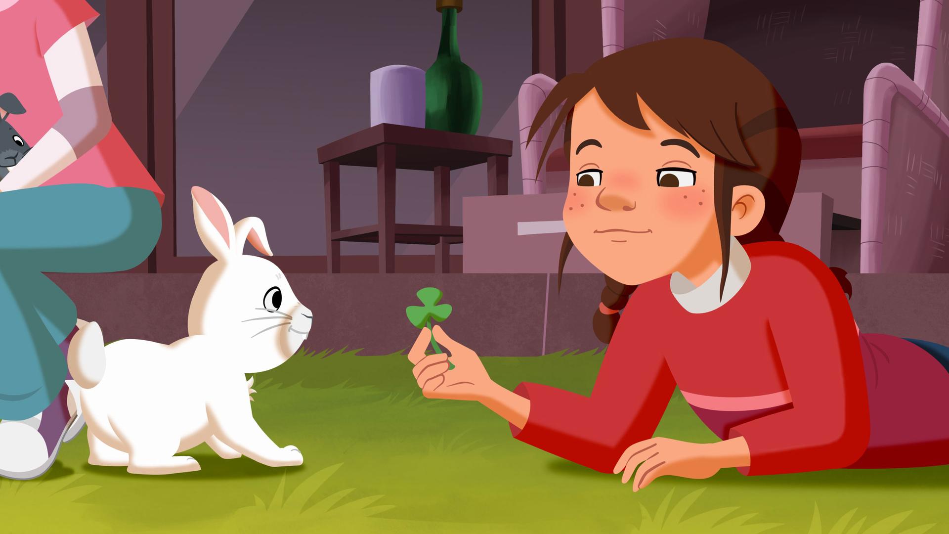 Tara spielt mit dem weißen Kaninchen und hält ihm ein Kleeblatt hin.