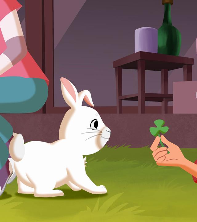 Tara spielt mit dem weißen Kaninchen und hält ihm ein Kleeblatt hin.