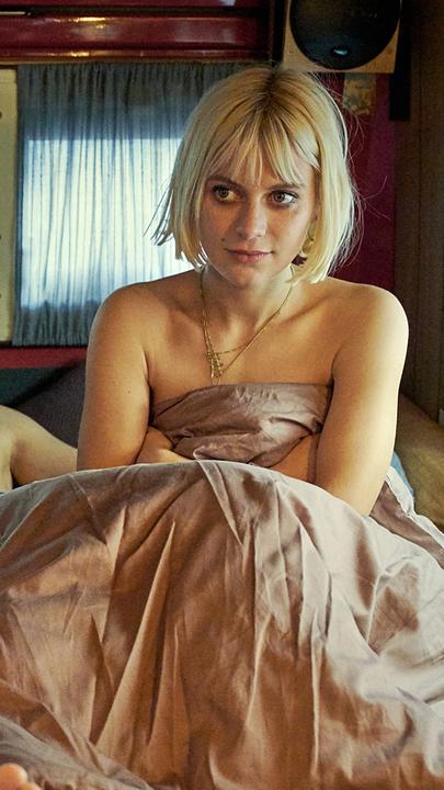 Liegender Sam (Kostja Ullmann) und sitzende Edda (Alli Neumann) nackt in Bettdecke gehüllt auf Bett im Wohnwagen.