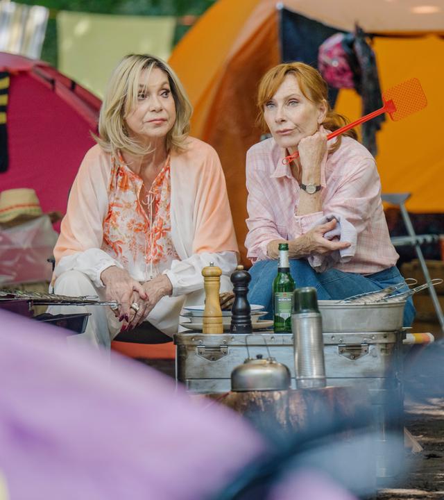 "Familie Bundschuh - Wir machen Camping": Susanne (Judy Winter, li) und Gundula (Andrea Sawatzki, re) sitzen zwischen Zelten und vor einem Grill und führen ein ernstes Gespräch.