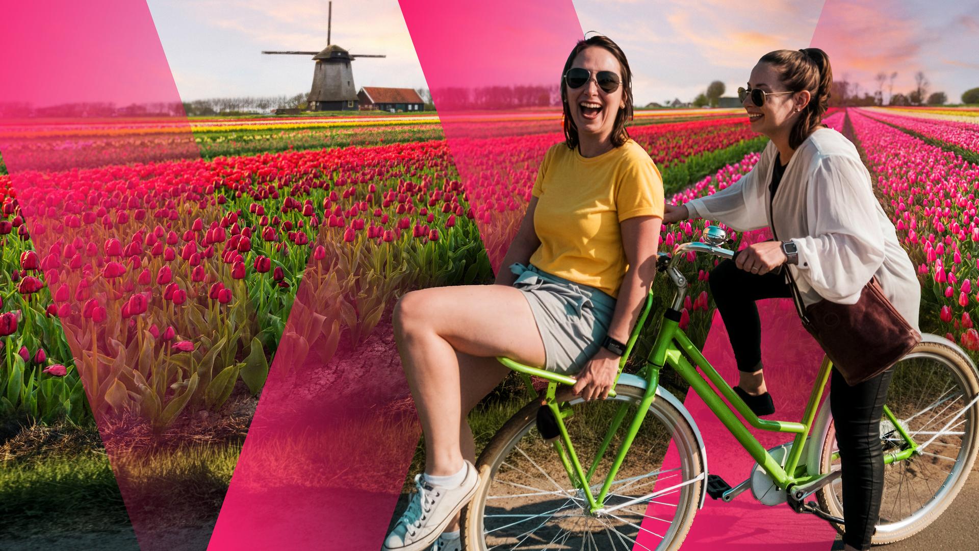 Zwei unbeschwerte, junge Frauen auf dem Fahrrad vor Tulpenfeld in den Niederlanden