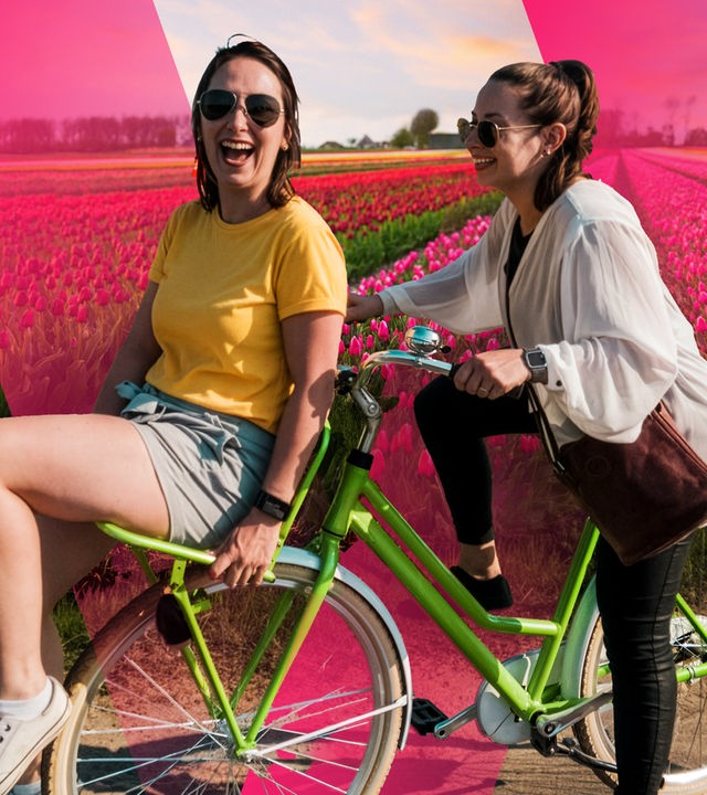 Zwei unbeschwerte, junge Frauen auf dem Fahrrad vor Tulpenfeld in den Niederlanden