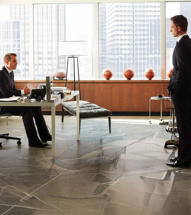 "Suits - Wissen, wann Schluss ist": Harvey (Gabriel Macht) sitzt an seinem Schreibtisch in einem hellen, modern eingerichteten Büro und blickt zu Mike (Patrick J. Adams), der mit ernster Miene im Raum steht. Im Hintergrund stehen mehrere Basketbälle auf einem Sideboard, dahinter ist die Skyline durch große Fenster zu sehen.