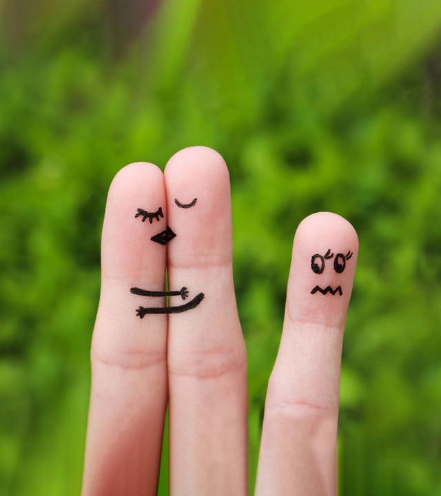 zwei Finger schmiegen sich aneinander, auf Ihnen die Gesichtsmimik von sich Küssenden aufgemalt, ein einzelner Finger mit aufgemalter unglücklicher Mimik im Abseits